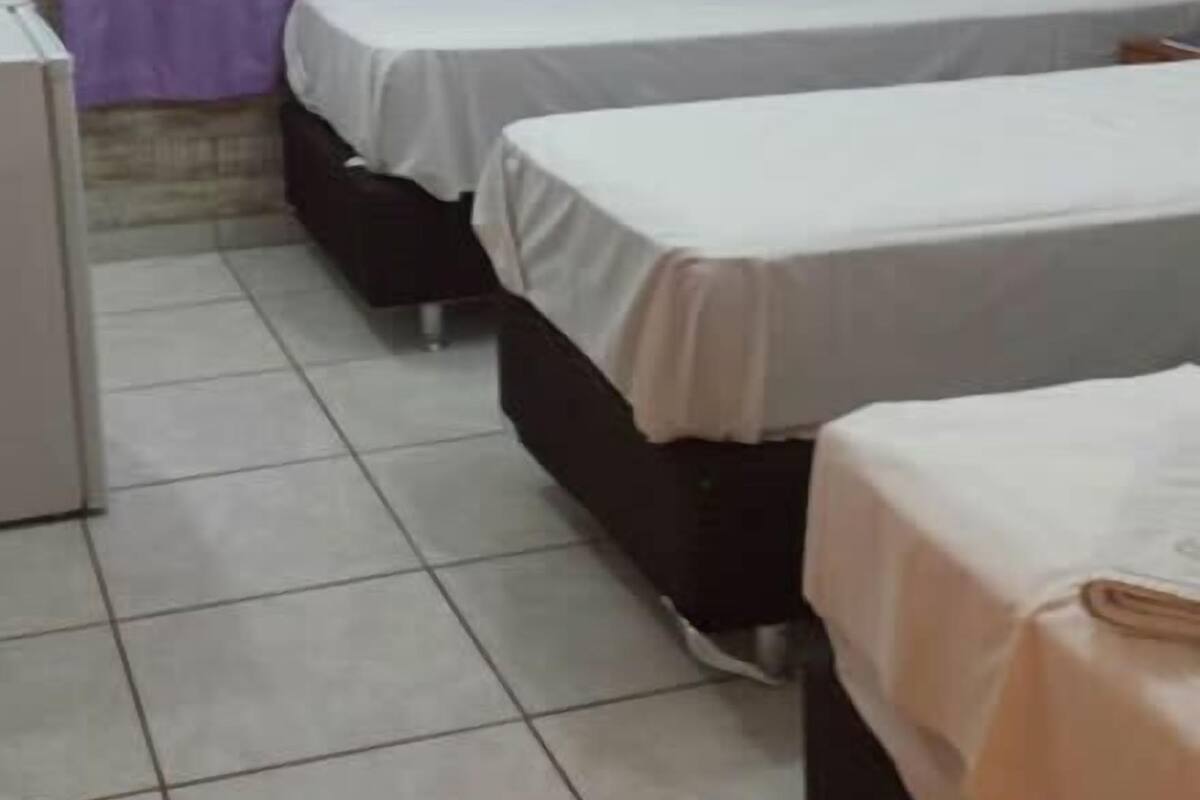 A room with two beds, a window with purple curtains, a tiled floor, and a white air conditioning unit on the wall.