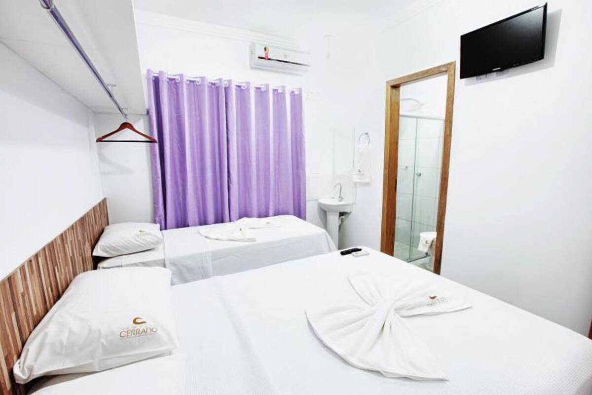 A hotel room with two beds, a bathroom, a TV, and a shower area.