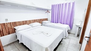 A hotel room with two beds, a wooden headboard, a bathroom with a sink, and a purple shower curtain. - Hotel Cerrado (Goiania)