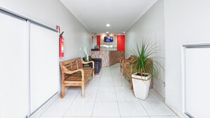 A hallway with wooden benches, a reception desk, a television, and a potted plant. - Hotel Cerrado (Goiania)