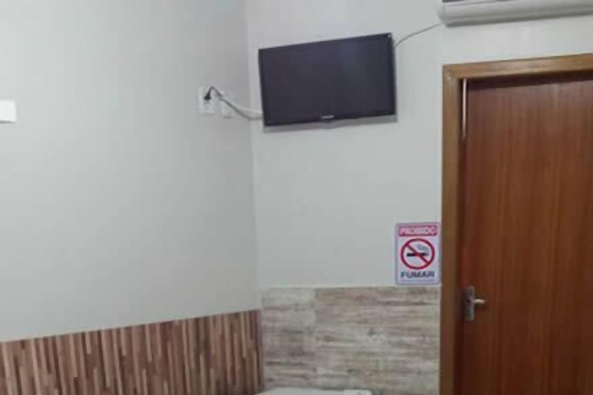 A hotel room with a bed, a TV mounted on the wall, a no-smoking sign, and a wooden door.