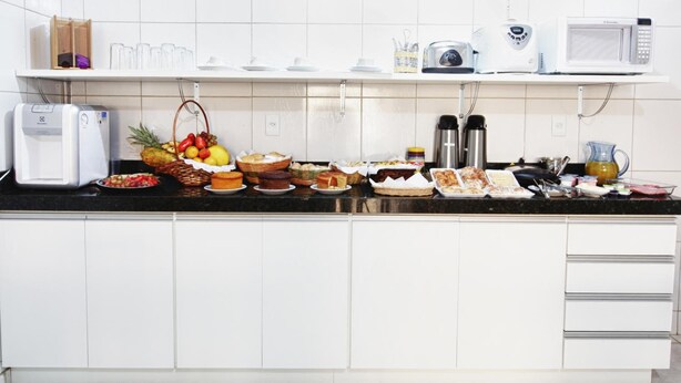 A kitchen with white cabinets, a black countertop, a microwave, and various food items. - Hotel Cerrado (Goiania)