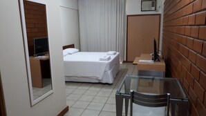 A hotel room with a bed, a desk, a television, a window, and a brick wall. - Hotel Sol da Praia (Vitoria)