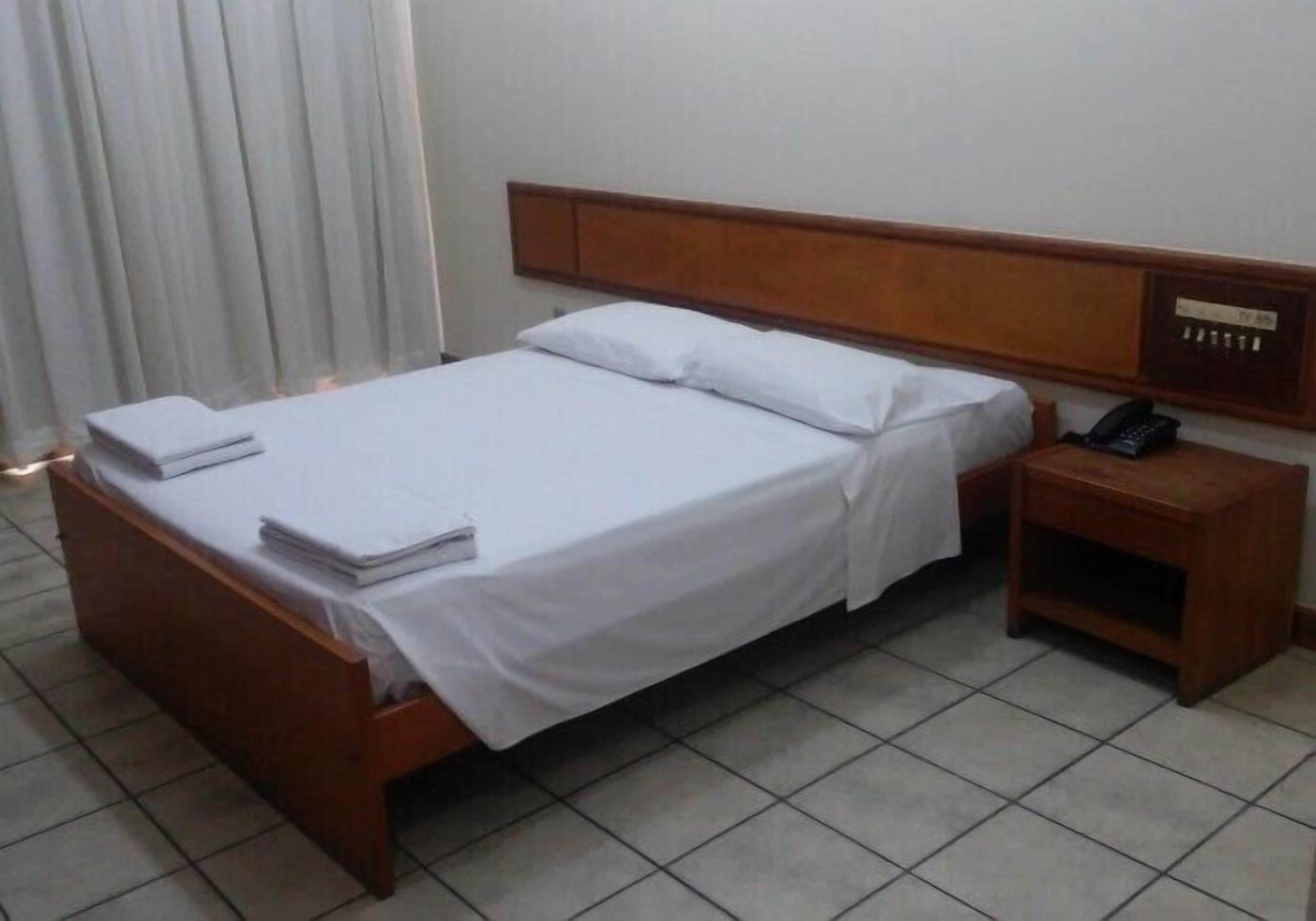 A hotel room with a wooden bed, white linens, a bedside table with a phone, and a curtain.