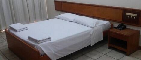 A hotel room with a wooden bed, white linens, a bedside table with a phone, and a curtain.