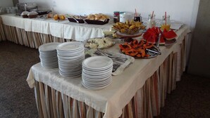 A buffet table with various food items and beverages, plates stacked on the side, and a white tablecloth. - Hotel Sol da Praia (Vitoria)