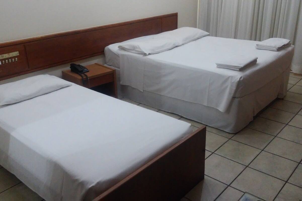 A hotel room with two single beds, a wooden headboard, a bedside table with a phone, and a curtain.