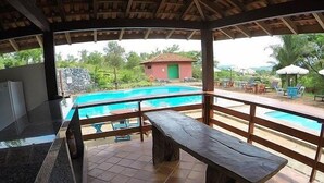 A covered outdoor area with a pool, wooden benches, and a view of a small building in the background. - Sesc Bonito (Bonito)