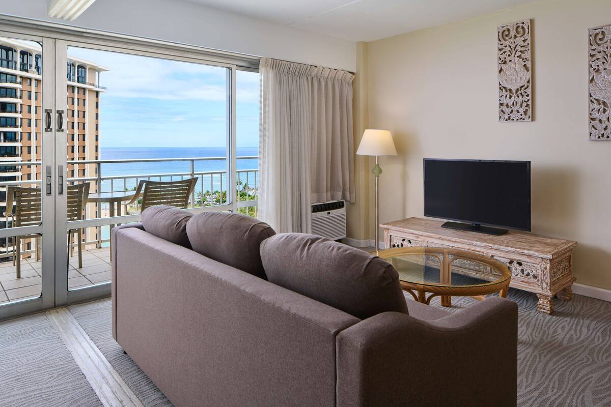 A hotel room with a balcony, a sofa, a television, and a decorative cabinet.