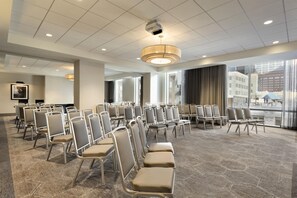 A conference room with rows of chairs, a large window with a view of buildings, and a ceiling with recessed lighting.