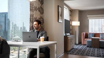 A modern hotel room with a desk, laptop, coffee cup, and a view of the cityscape.