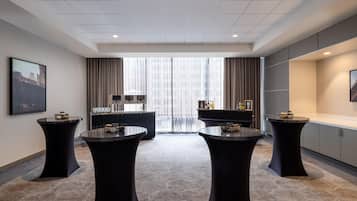 A hotel room with a large window, a minibar, a flat-screen TV, and a round table with a black tablecloth.