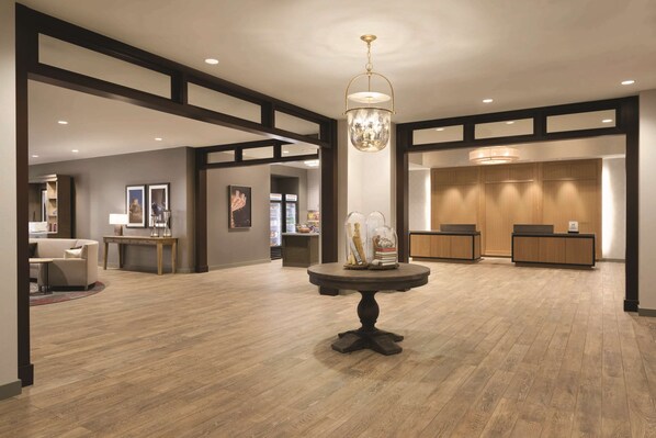 Un hall d’entrée spacieux doté d’un plancher en bois, une table ronde centrale agrémentée d’objets décoratifs, un comptoir de réception et des œuvres d’art encadrées qui ornent les murs.