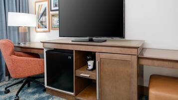 A hotel room with a flat-screen TV, a mini-fridge, a coffee maker, and an orange chair.