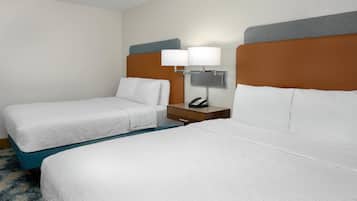 Habitación de hotel con dos camas, una mesita de noche con lámpara y teléfono, y piso alfombrado.