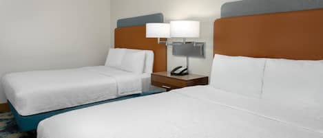 A hotel room with two beds, a nightstand with a lamp and phone, and a carpeted floor.