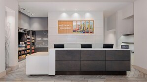 Zona de recepción de hotel con diseño moderno, que incluye un mostrador de recepción, un cartel de bienvenida y una exhibición de atractivos locales.