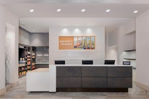 A reception desk with a 'Welcome to Hampton' sign, a cityscape artwork, and a 'Hilton Honors' plaque.