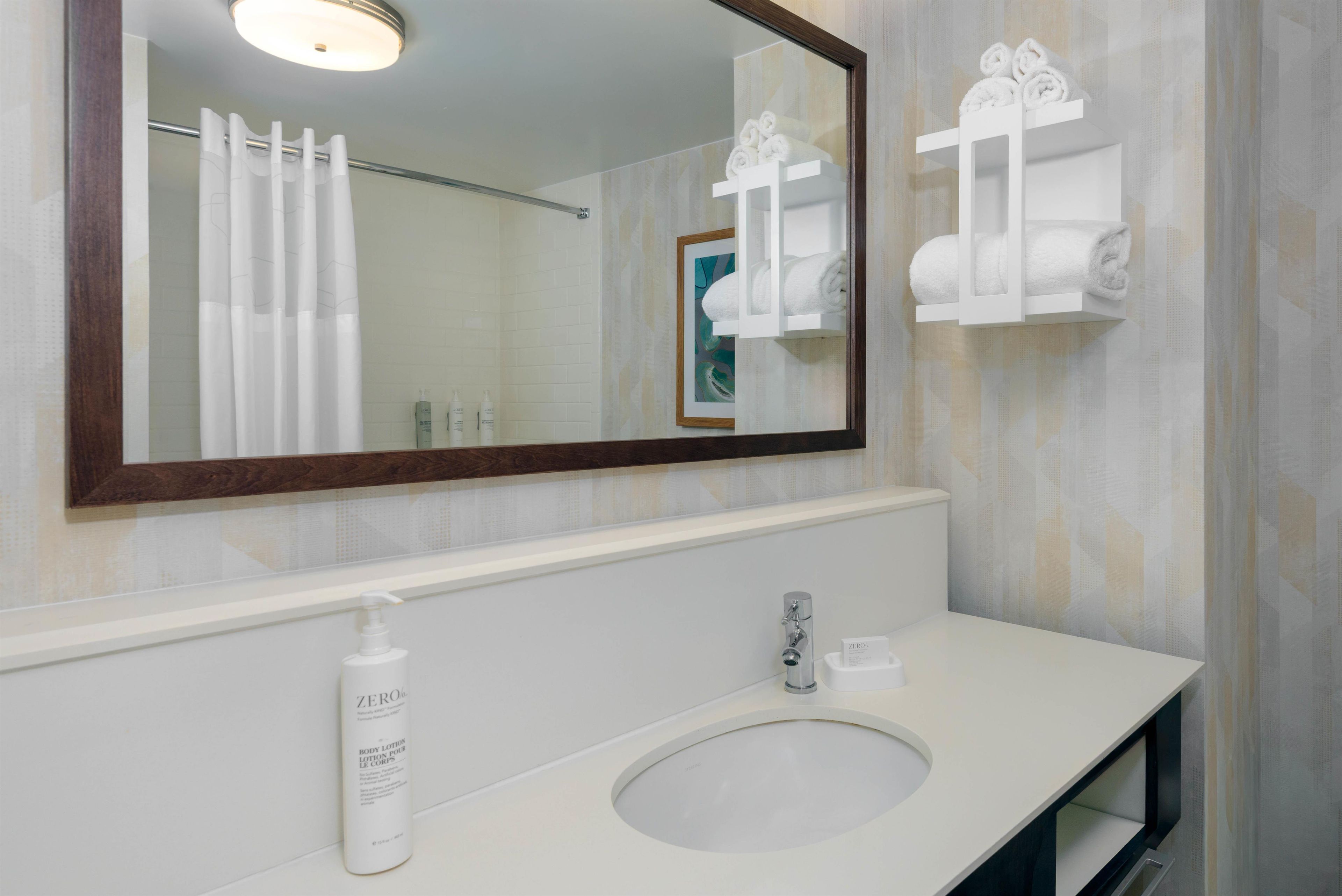 Un baño con un lavamanos blanco, un espejo con marco de madera y un perchero con toallas.
