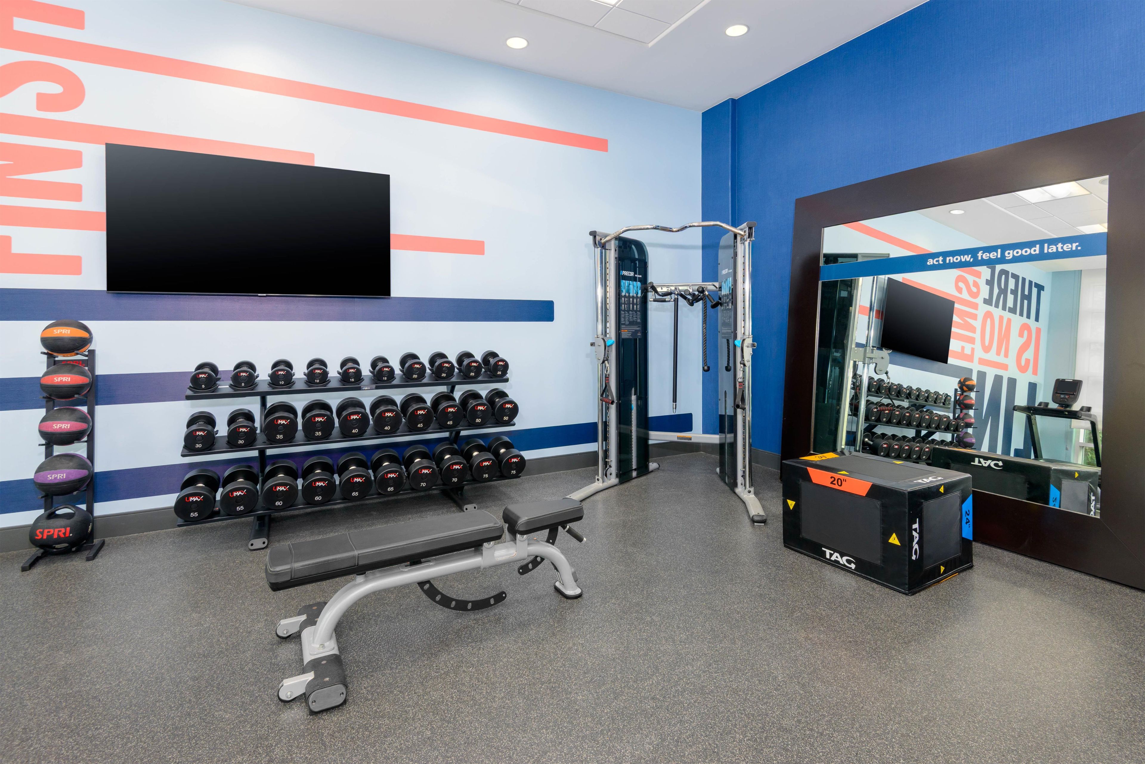 Ein Fitnessraum mit Gewichtstrainern, einer Bank und einem an der Wand montierten Fernseher.