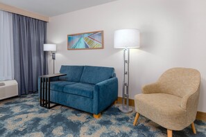 A hotel room with a blue sofa, a beige armchair, a floor lamp, a standing lamp, and a painting on the wall. - Hampton Inn & Suites Tampa Airport Avion Park Westshore (Tampa)