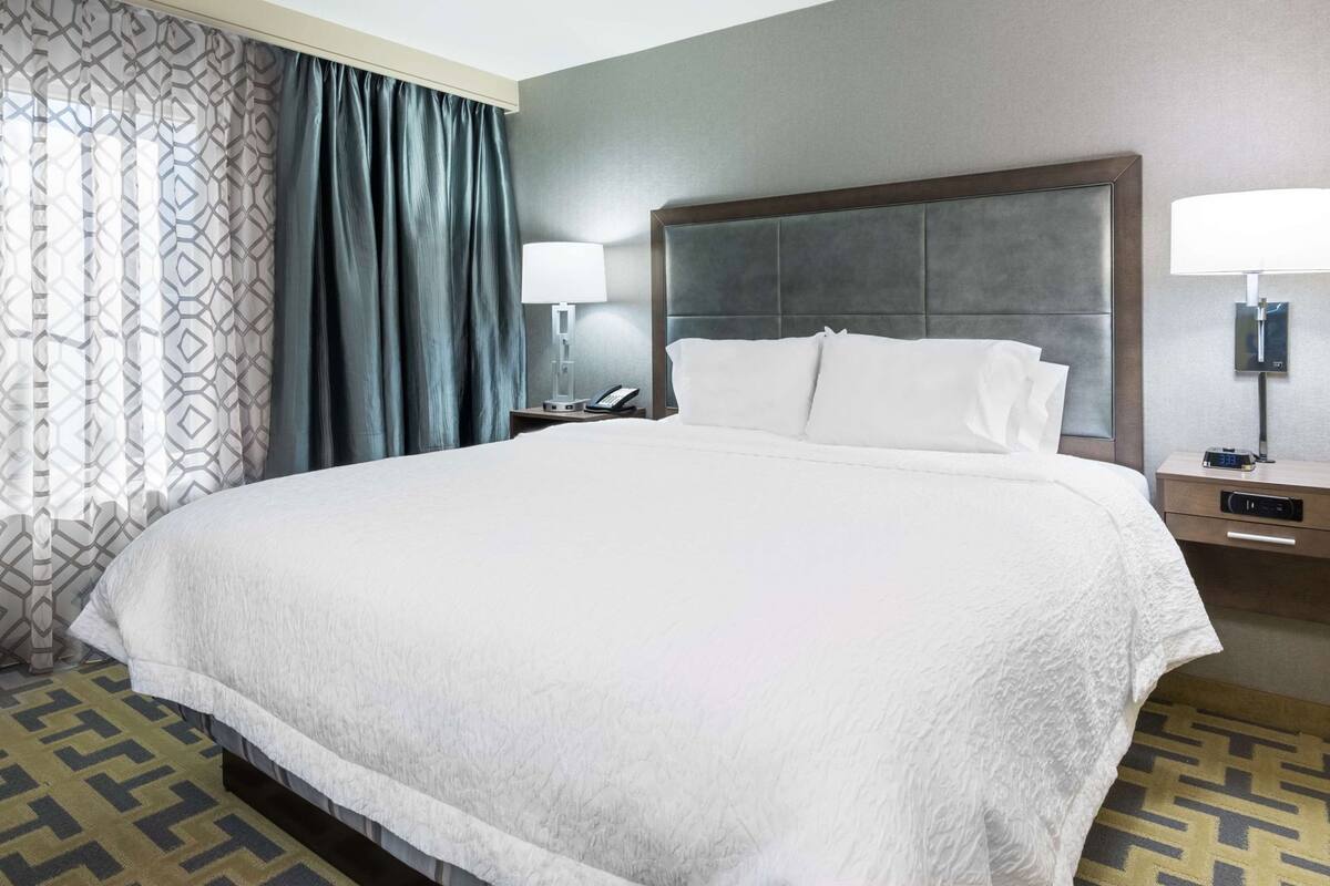 Une chambre d’hôtel avec un grand lit, une table de chevet avec une lampe, un téléphone et une horloge numérique.