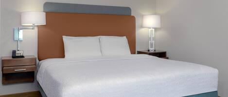 A neatly made bed with white linens, a wooden nightstand with a lamp, and a wall-mounted lamp.