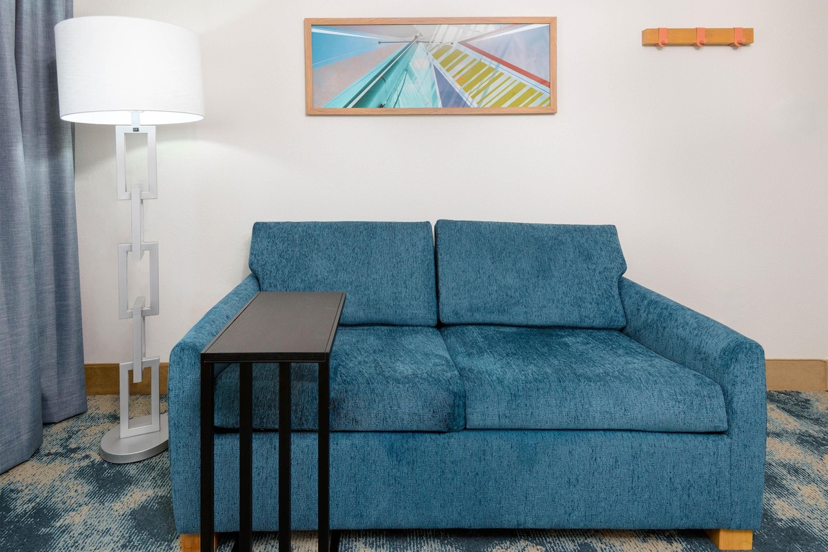 Ein blaues Sofa mit einem kleinen Tisch, einer Stehlampe und einem gerahmten Bild an der Wand.