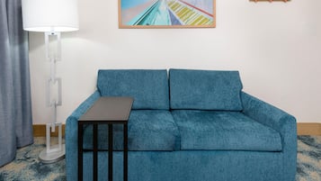 Un sofá azul con una mesita, una lámpara de pie y un cuadro en la pared.