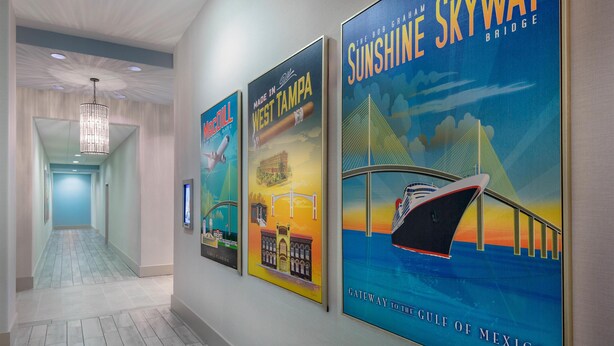 Un pasillo con tres carteles de viajes en la pared, que muestran el Puente Sunshine Skyway y la ciudad de West Tampa.