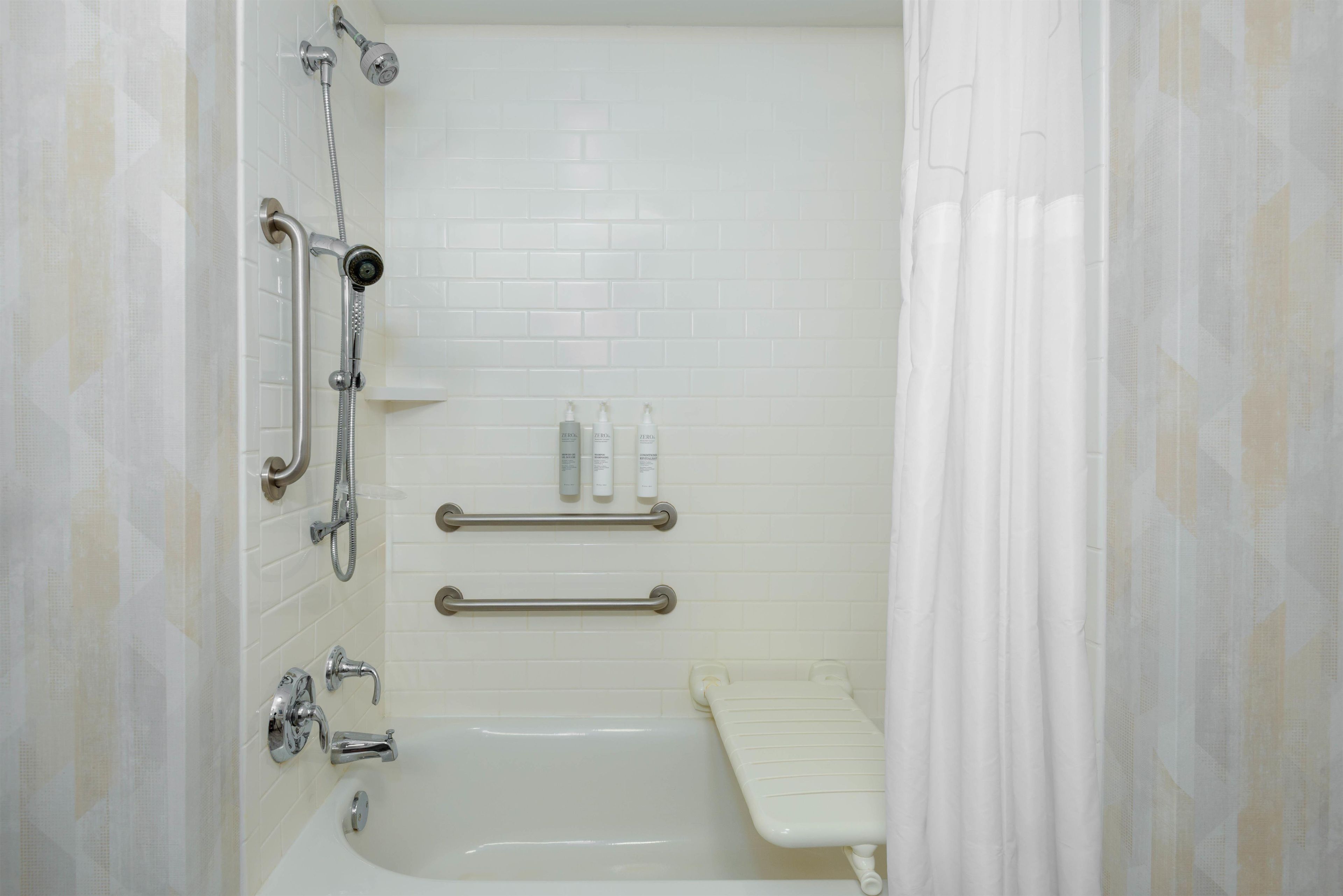 Une salle de bain équipée d’une baignoire, d’une douche et de toilettes. On y trouve également des barres d’appui et un porte-serviettes.