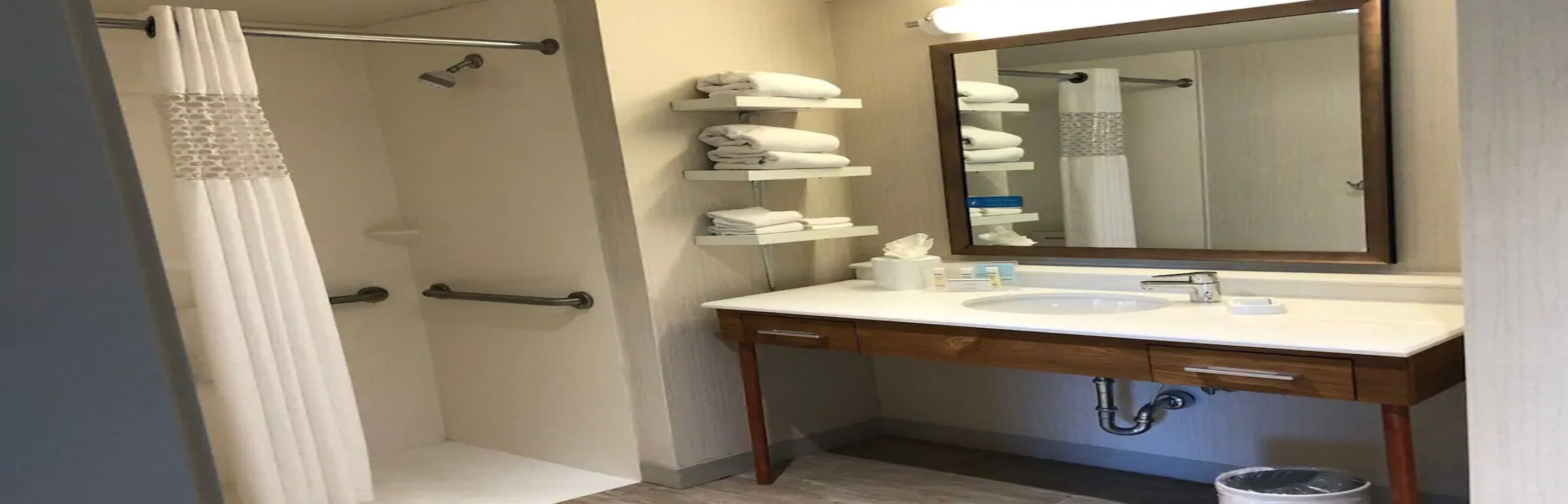 A bathroom with a shower, a sink, a mirror, and shelves with towels.