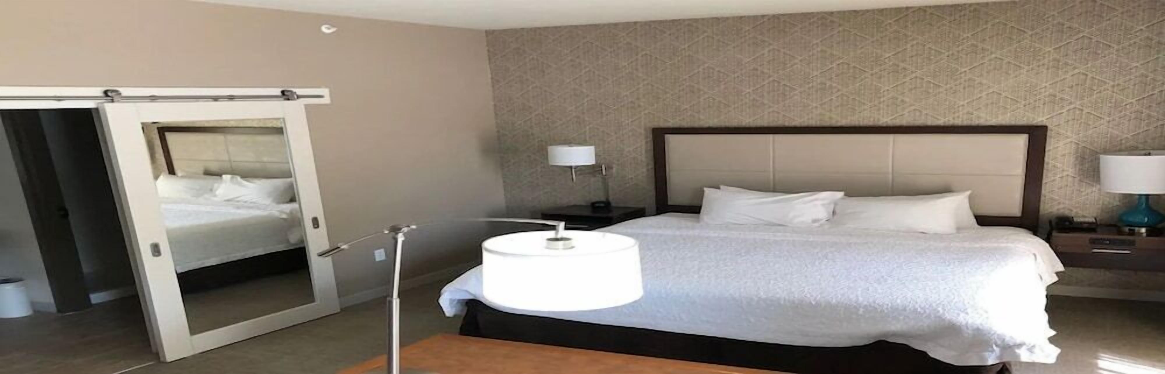 A hotel room with a bed, a nightstand, a lamp, and a mirror.