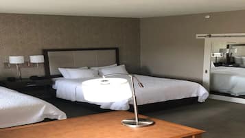 A hotel room with two beds, a bedside table, a lamp, and a sliding door leading to a bathroom.