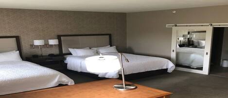 A hotel room with two beds, a bedside table, a lamp, and a sliding door leading to a bathroom.