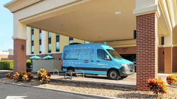 Una camioneta azul estacionada bajo una estructura cubierta con un pilar de ladrillo y un banco.