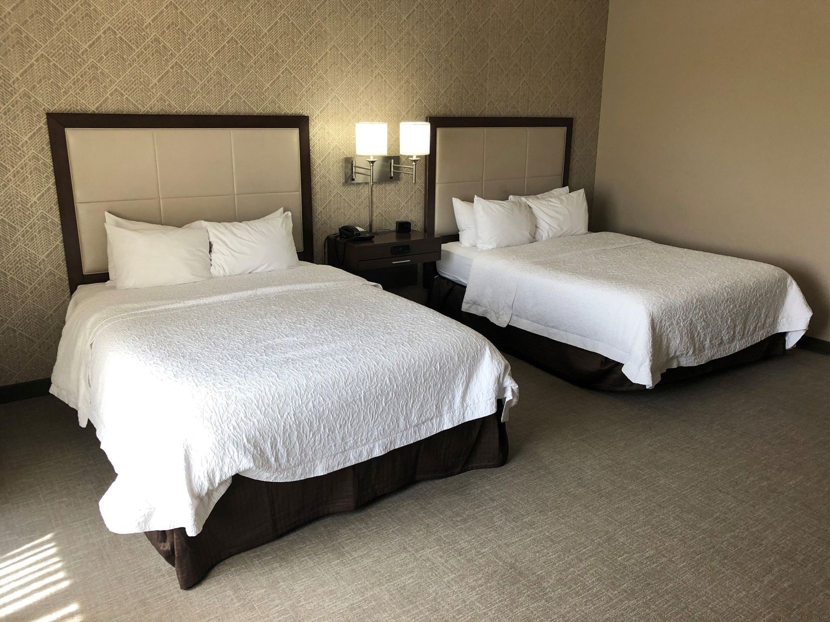 Two beds with headboards, a nightstand with a lamp, and a patterned wall.