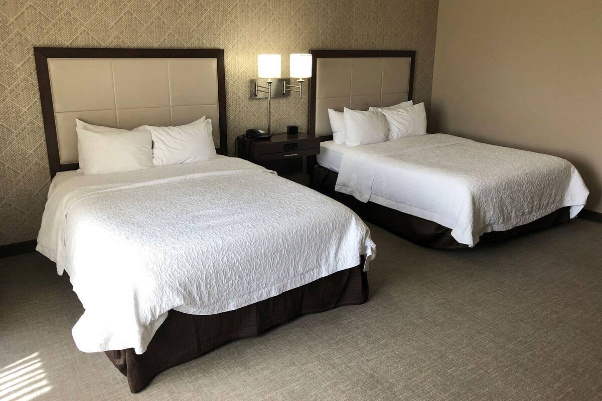 Two beds with headboards, a nightstand with a lamp, and a patterned wall.