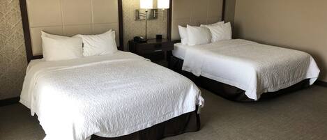 A hotel room with two beds, a nightstand, and a wall-mounted lamp.