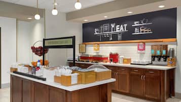 En morgenmadsbuffet med et skilt der viser, hvor morgenmaden serveres, en kaffestation og en tavle med ordene "HAPPY BREAKFAST STARTS HERE".