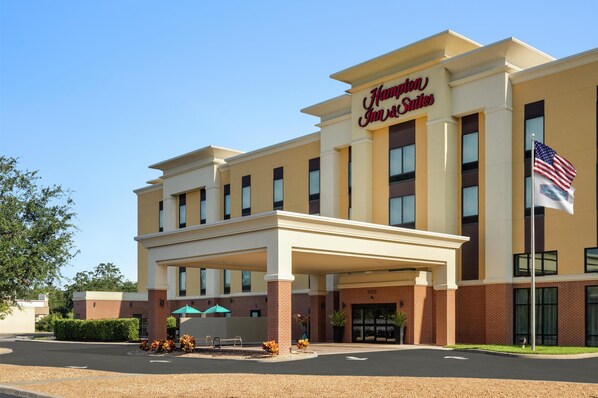 A Hampton Inn Suites building with a covered entrance, American flags, and a clear blue sky. - Hampton Inn & Suites Tampa Busch Gardens Area (Tampa)