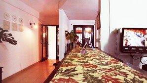 A hallway with a patterned carpet, a television on the right, and a door at the end. - Costanera Hostel Asuncion (Asunción)