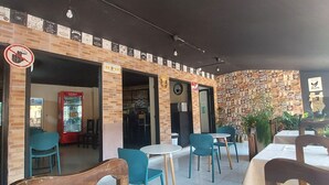 An outdoor cafe with brick walls, blue chairs, and tables. There are signs on the walls and a no-smoking sign. - Costanera Hostel Asuncion (Asunción)