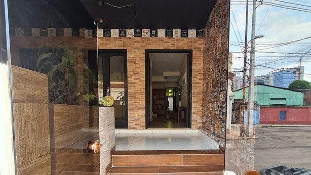 A modern building entrance with a glass door, a brick wall, and a tiled floor leading to a hallway. - Costanera Hostel Asuncion (Asunción)