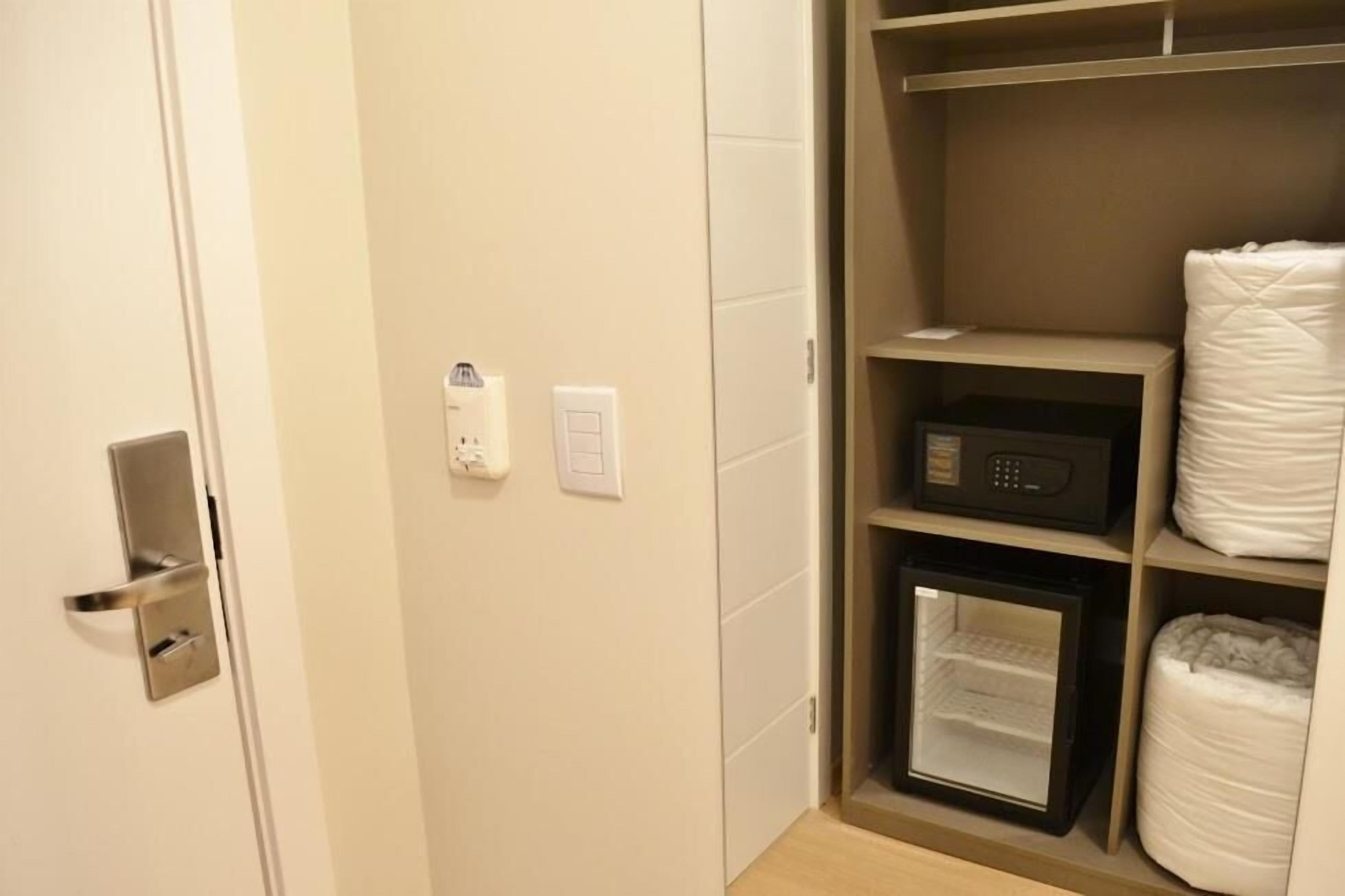 Habitación de hotel con puerta, termostato, microondas y armario.