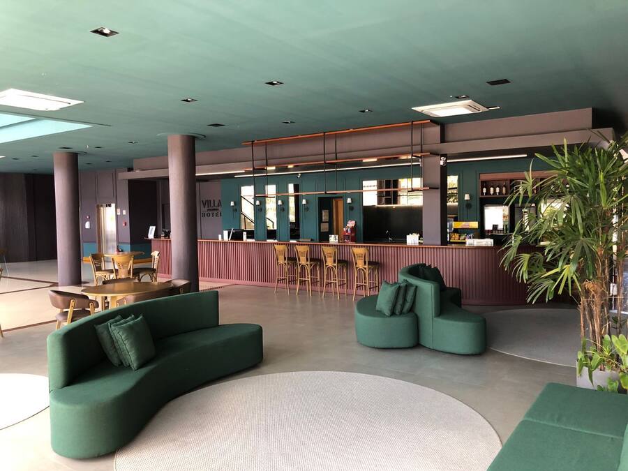 A modern hotel lobby with a bar area, seating arrangements, and a large potted plant.