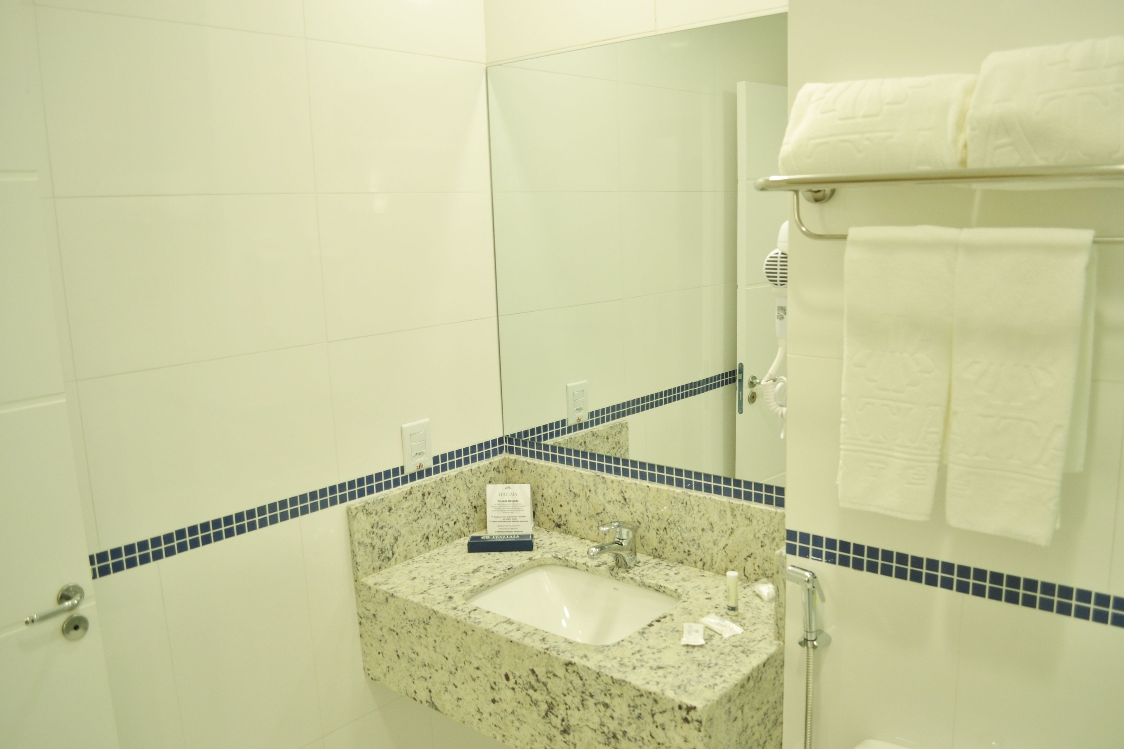 Ein Badezimmer mit Waschbecken, Spiegel, Handtuchhalter und einem Schild an der Wand.