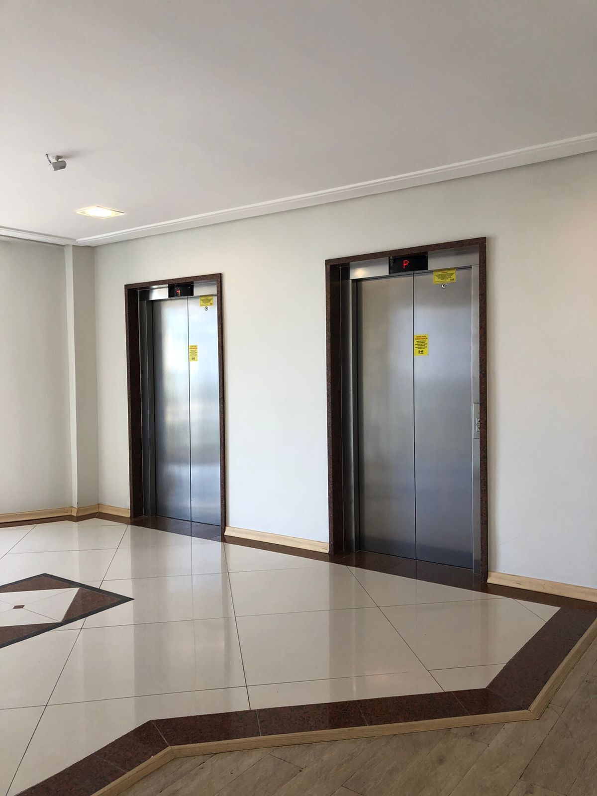 Dos puertas de ascensor en un pasillo con suelo de baldosas y paredes lisas.