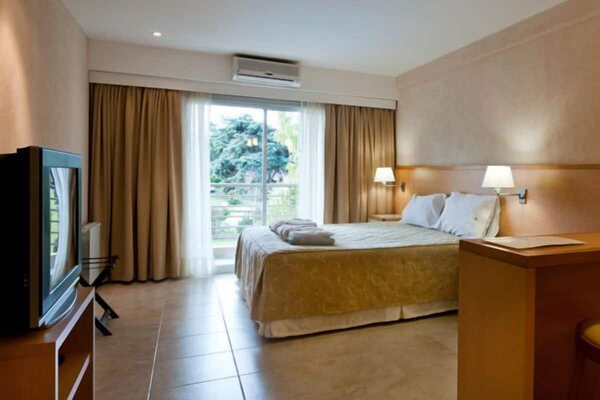 A hotel room with a bed, a TV, a desk, and a window with curtains.