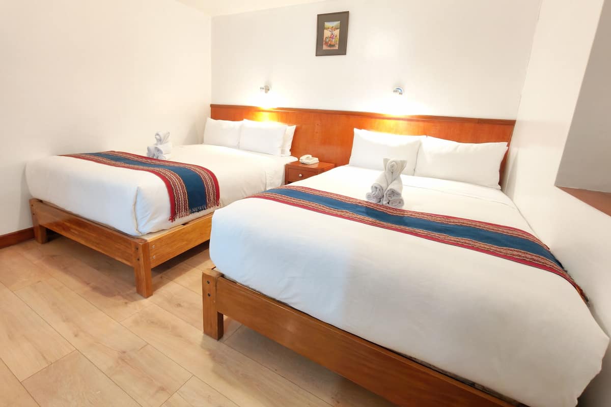 Two wooden beds with white bedding and red and blue striped blankets, a wooden headboard, and a small bedside table with a phone.